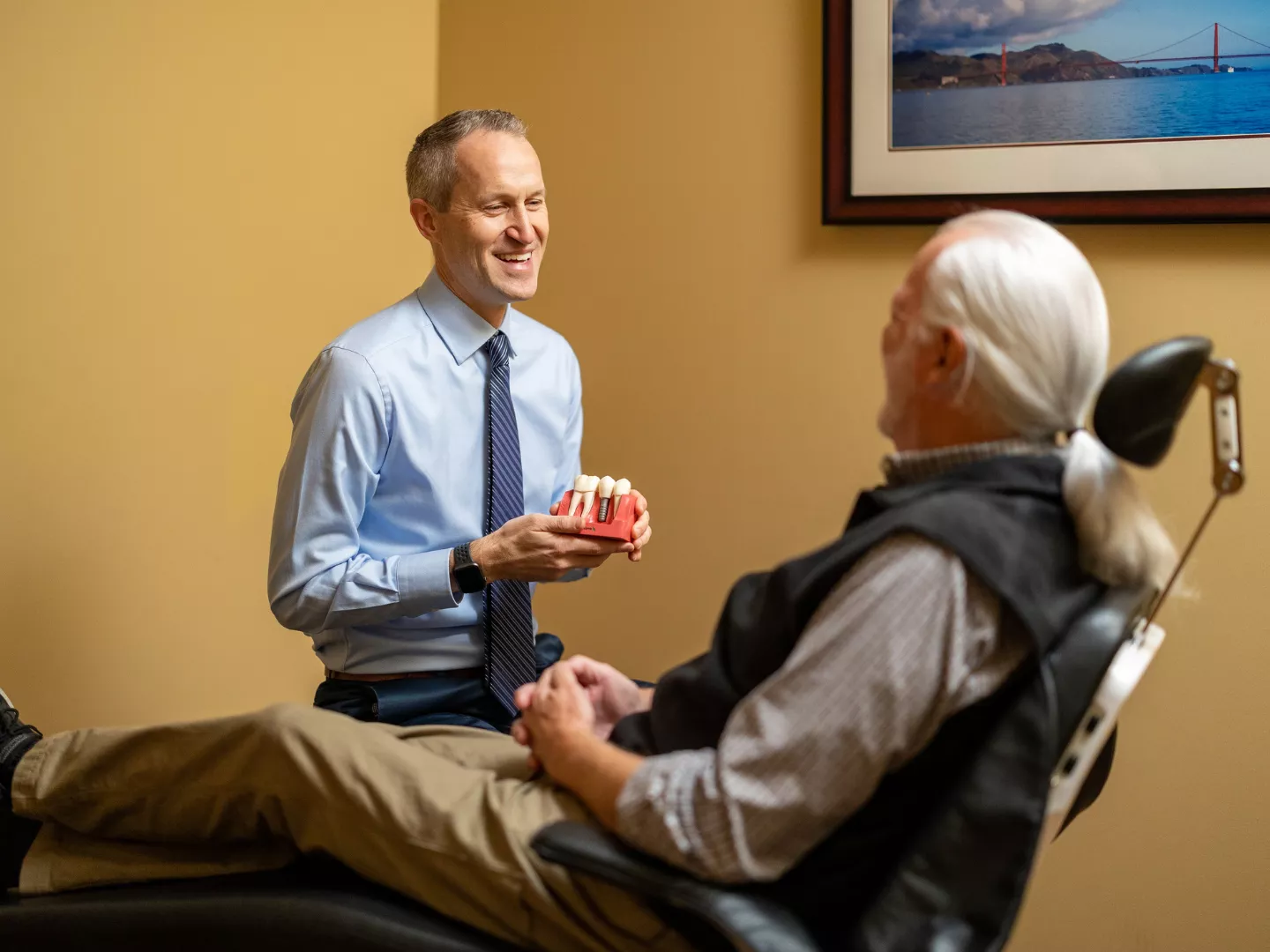 Dr. Young smiles holding a dental implant model in a consult with a patient.
