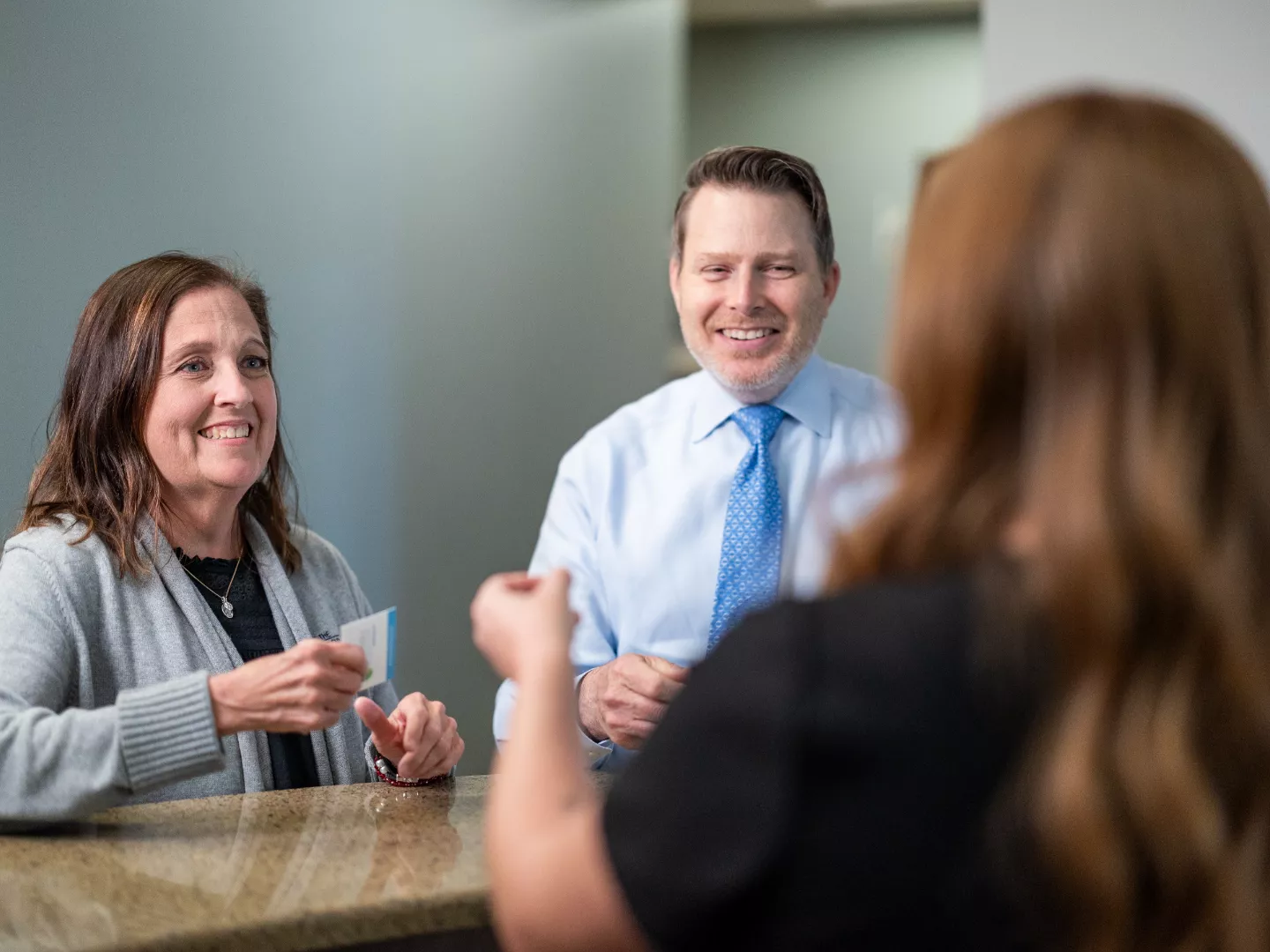 Dr. Clark smiles at the reception desk with a patient and team member.