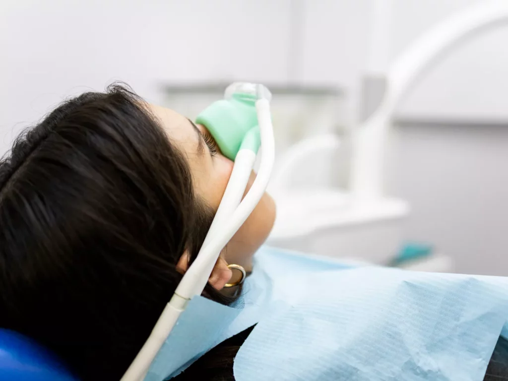 A woman sits comfortably being administered sedation wearing a sedation mask.