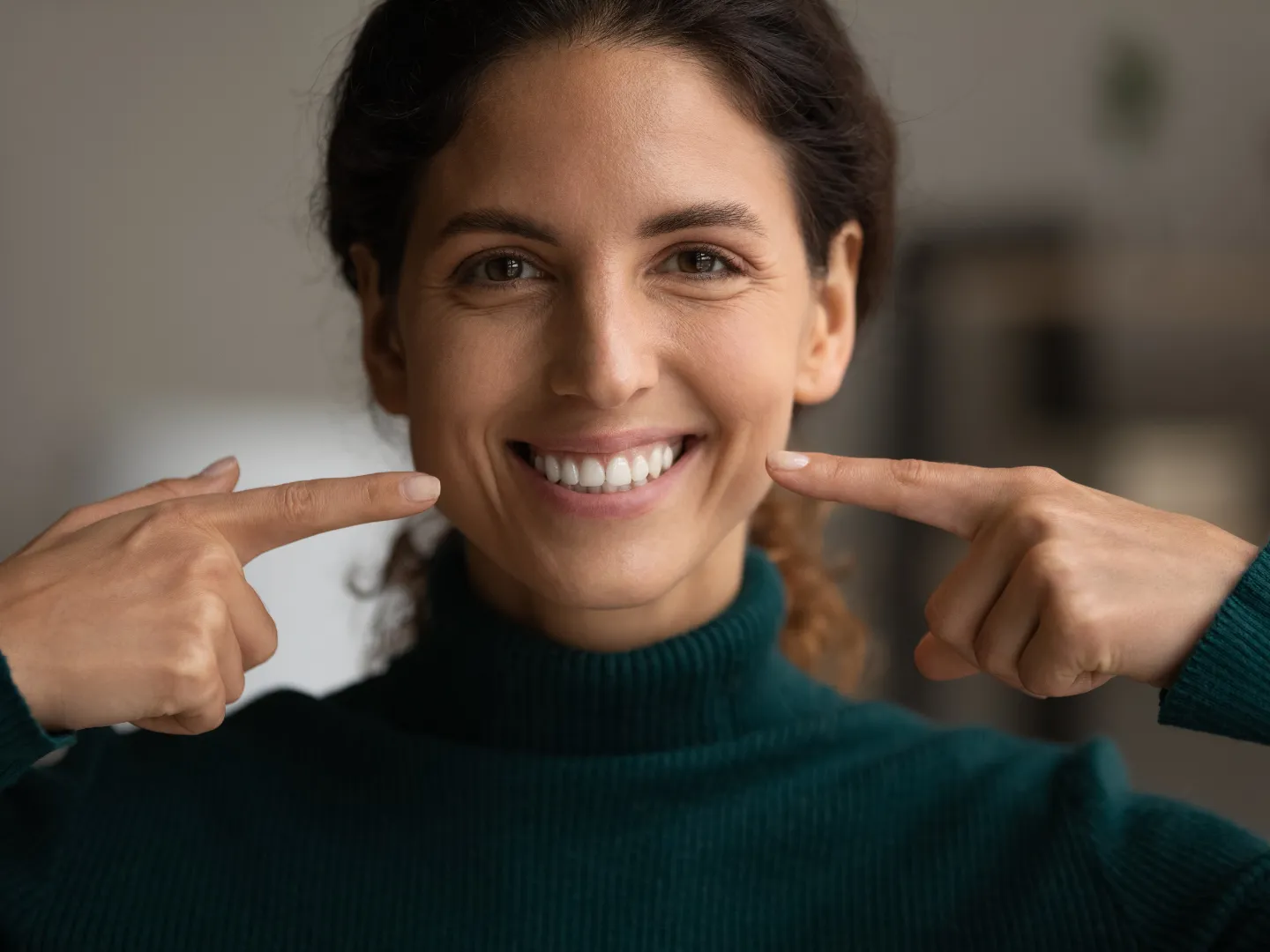 A woman smiling comfortably and pointing to her teeth.